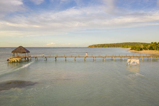 Aerial view of a couple walking on a wooden pier near a luxury resort at sunset in Puerto Plata state Villa Isabela Dominican Republic.