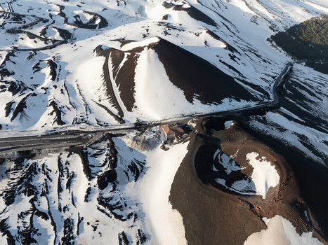 Aerial view of the snow covered volcanic craters on the south side of Mount Etna with winding roads and dark volcanic ash in Nicolosi Sicilia Italy. Aerial view of the snow covered volcanic craters on the south side of Mount Etna with winding roads and dark volcanic ash in Nicolosi Sicilia Italy.
