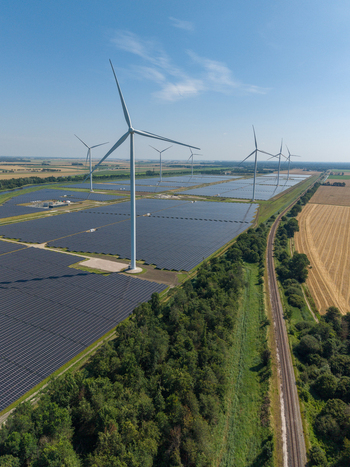 Aerial view of a large solar farm with wind turbines rows of solar panels green trees and a railway track Netherlands.
