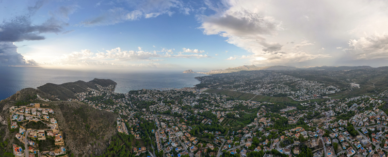Aerial view of the coastal town of Moraira featuring residential areas lush hills the Mediterranean Sea and a dramatic cloudy sky in Moraira Valencian Community Spain.