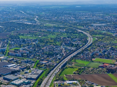 Aerial view of a long winding highway cutting through a vibrant landscape of green fields and dense urban development Sausheim Grand Est France.