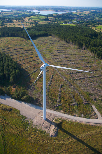 Aerial view of a lone wind turbine standing tall against a backdrop of dark green forest and distant blue lake Salles Curan Occitanie France. Aerial view of a lone wind turbine standing tall against a backdrop of dark green forest and distant blue lake Salles Curan Occitanie France.