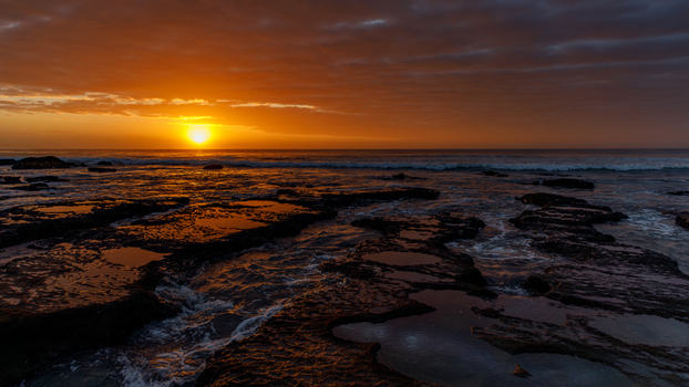 Aerial view of Hartenbos coastline with a golden sunset over the ocean rocky tide pools reflecting the sky and gentle waves Mossel Bay Western Cape South Africa.
