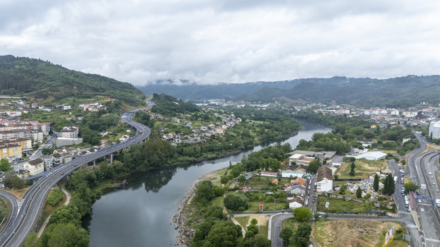 Aerial view of the Minho River flowing through the city with a winding highway bridge and lush green hills under a cloudy sky in Ourense Province of Ourense Spain.