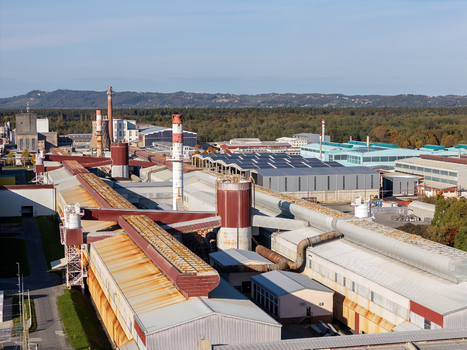 Aerial view of a large industrial complex with factory buildings tall chimneys and extensive piping systems surrounded by green forests Slovenia. Aerial view of a large industrial complex with factory buildings tall chimneys and extensive piping systems surrounded by green forests Slovenia.