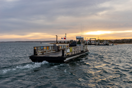 View of the Chappy Ferry in Martha s Vineyard with a person in the booth crossing the water towards the dock at sunset Edgartown Massachusetts United States.