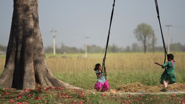 View of children playing on a swing under a large tree Nepal.