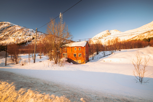 View of a vibrant red building stands out against the pristine white snow under a clear blue sky framed by snow dusted mountains Indregård Norway. View of a vibrant red building stands out against the pristine white snow under a clear blue sky framed by snow dusted mountains Indregård Norway.
