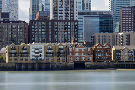 View of the Thames waterfront featuring a mix of modern glass skyscrapers and historic brick buildings along the riverbank in London England United Kingdom. View of the Thames waterfront featuring a mix of modern glass skyscrapers and historic brick buildings along the riverbank in London England United Kingdom.