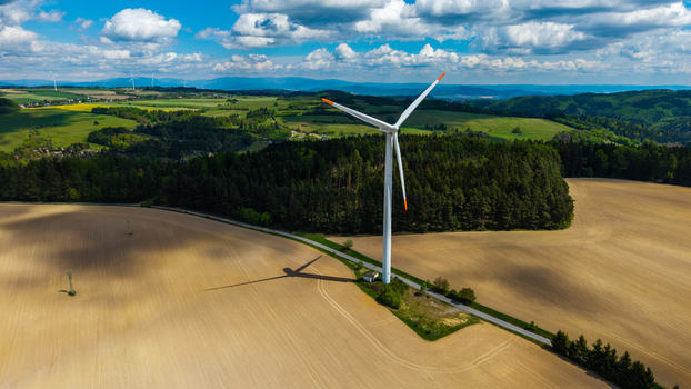 Aerial view of the Zipotin wind turbine standing amidst rolling green hills dense forests and vast agricultural fields under a cloudy sky in Gruna Pardubicky kraj Czechia. Aerial view of the Zipotin wind turbine standing amidst rolling green hills dense forests and vast agricultural fields under a cloudy sky in Gruna Pardubicky kraj Czechia.