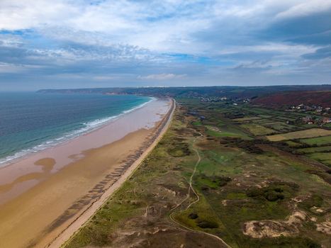 Aerial view of Dunes de Biville featuring a sandy beach rolling green fields and the coastline in La Hague Normandie France.