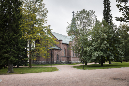 View of the historic brick Jyvaskyla City Church surrounded by lush green trees and a gravel path in Jyvaskyla Central Finland Finland.