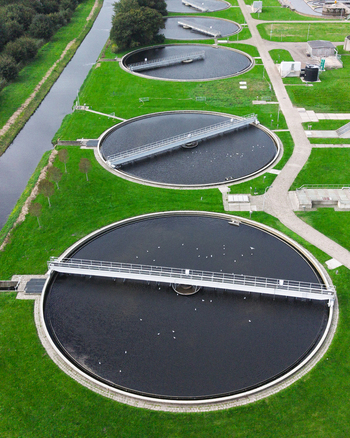 Aerial view of a wastewater treatment plant featuring large circular sedimentation tanks with metal bridges surrounded by green grass and a canal in Warmenhuizen North Holland Netherlands. Aerial view of a wastewater treatment plant featuring large circular sedimentation tanks with metal bridges surrounded by green grass and a canal in Warmenhuizen North Holland Netherlands.