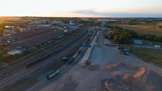 Aerial view of Wellingborough sidings freight terminal at sunset with freight trains on tracks industrial warehouses and piles of aggregate in Wellingborough England United Kingdom. Aerial view of Wellingborough sidings freight terminal at sunset with freight trains on tracks industrial warehouses and piles of aggregate in Wellingborough England United Kingdom.