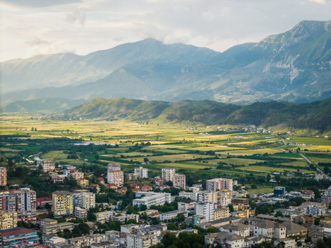 Aerial view of the historic city of Gjirokaster with its residential buildings overlooking a lush green valley and the rugged mountain range in Gjirokaster Gjirokaster County Albania. Aerial view of the historic city of Gjirokaster with its residential buildings overlooking a lush green valley and the rugged mountain range in Gjirokaster Gjirokaster County Albania.