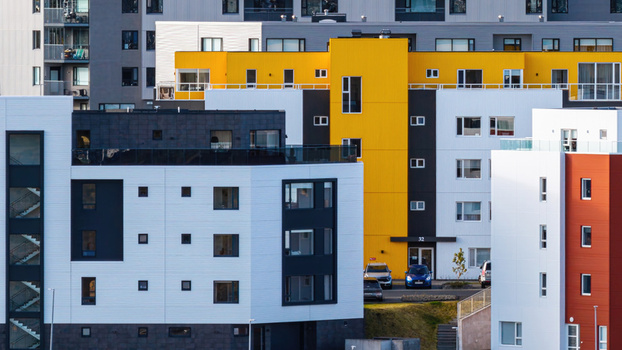 Aerial view of a modern apartment complex with vibrant yellow white and red facades featuring clean architectural lines and parked cars in the foreground in Iceland. Aerial view of a modern apartment complex with vibrant yellow white and red facades featuring clean architectural lines and parked cars in the foreground in Iceland.