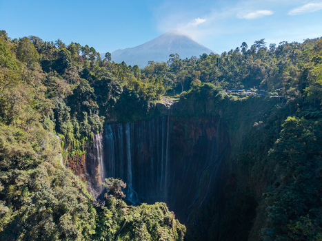 Aerial view of Tumpak Sewu Waterfall cascading into a lush canyon with Mount Semeru volcano in the background in Kecamatan Pronojiwo Jawa Timur Indonesia.