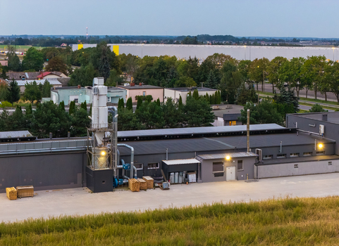 Aerial view of an industrial facility with a prominent ventilation chimney stacks of wooden materials and a large warehouse building surrounded by trees in Greater Poland Voivod Poland.