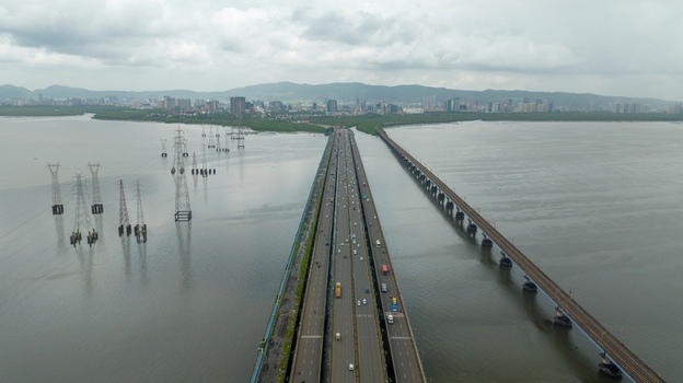 Aerial view of Vashi bridge spanning the creek with traffic electricity pylons in the water and the city skyline in Navi Mumbai Maharashtra India.