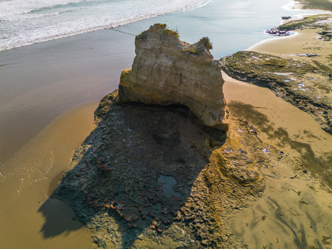 Aerial view of a prominent rock formation on a sandy beach with ocean waves crashing nearby in Bali Bali Indonesia. Aerial view of a prominent rock formation on a sandy beach with ocean waves crashing nearby in Bali Bali Indonesia.