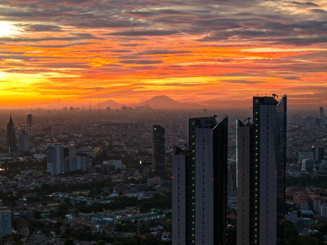 Aerial view of Jalan Jendral Sudirman skyscrapers during a vibrant sunset with distant mountains in the background in Kecamatan Setiabudi Daerah Khusus Ibukota Indonesia. Aerial view of Jalan Jendral Sudirman skyscrapers during a vibrant sunset with distant mountains in the background in Kecamatan Setiabudi Daerah Khusus Ibukota Indonesia.