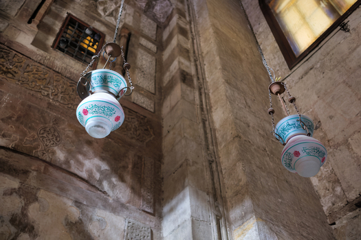 View of ornate hanging mosque lamps and intricate Islamic calligraphy on the stone walls of the Sultan al Ghuri Complex El Darb El Ahmar Cairo Governorate Egypt. View of ornate hanging mosque lamps and intricate Islamic calligraphy on the stone walls of the Sultan al Ghuri Complex El Darb El Ahmar Cairo Governorate Egypt.