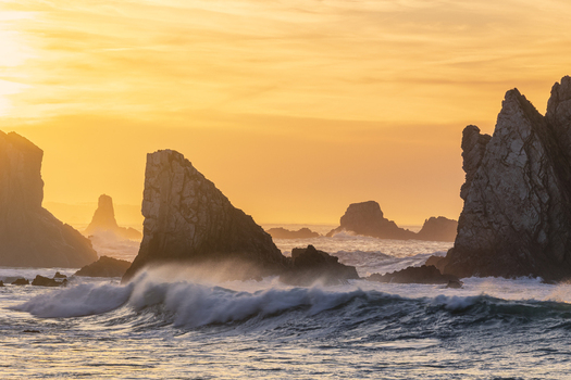 View of Silence Beach featuring jagged sea stacks and crashing waves under a vibrant golden sunset sky in Asturias Asturias Spain.