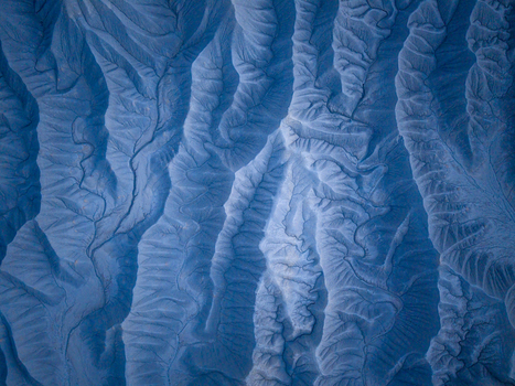 Aerial view of the intricate eroded badlands of the Caineville desert featuring deep ridges sharp gullies and textured blue toned earth formations in Caineville Utah United States. Aerial view of the intricate eroded badlands of the Caineville desert featuring deep ridges sharp gullies and textured blue toned earth formations in Caineville Utah United States.