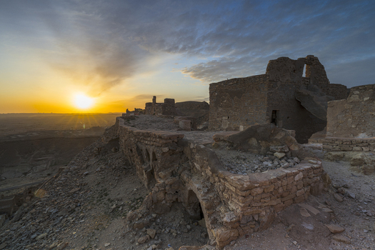 View of the historic stone ruins of a Ksar at sunset with golden light illuminating the ancient walls and the desert landscape in Tataouine Tataouine Governorate Tunisia.