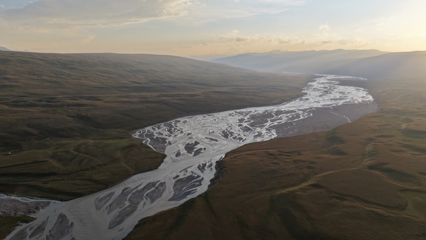 Aerial view of the Enilchek River with its intricate braided channels flowing through the vast mountainous valley during golden hour in Enilchek Issyk Kul Region Kyrgyzstan. Aerial view of the Enilchek River with its intricate braided channels flowing through the vast mountainous valley during golden hour in Enilchek Issyk Kul Region Kyrgyzstan.