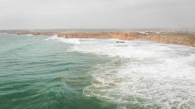 Aerial view of the rugged cliffs of Sagres and crashing waves of the Atlantic Ocean under an overcast sky in Sagres Faro Portugal. Aerial view of the rugged cliffs of Sagres and crashing waves of the Atlantic Ocean under an overcast sky in Sagres Faro Portugal.