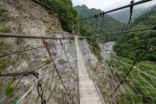 View of Taroko National Park suspension bridge spanning a deep rocky gorge with lush green mountains and a river flowing below in Xiulin Township Hualien County Taiwan.