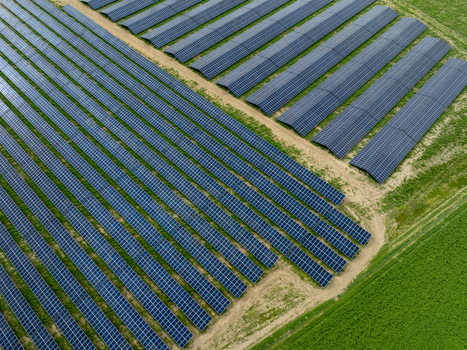 Aerial view of rows of blue solar panels installed on a green field with dirt paths.