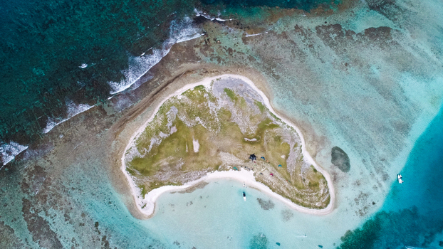 Aerial view of Los Roques archipelago featuring a small island with white sand beaches lush green vegetation and surrounding turquoise coral reefs in Los Roques Dependencias Federale Venezuela. Aerial view of Los Roques archipelago featuring a small island with white sand beaches lush green vegetation and surrounding turquoise coral reefs in Los Roques Dependencias Federale Venezuela.