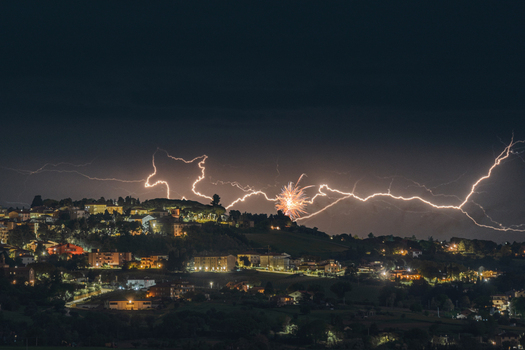 View of lightning strikes and fireworks illuminating the night sky over the historic town of Morrovalle Marche Italy.