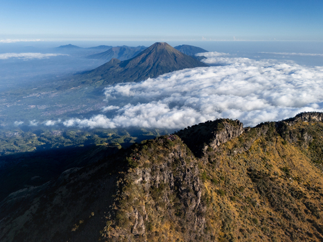 Aerial view of Mount Sumbing rising above a sea of clouds with rugged volcanic terrain and lush green valleys in Kecamatan Kalikajar Jawa Tengah Indonesia.