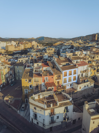 Aerial view of colorful traditional houses with terracotta rooftops and narrow streets against a backdrop of distant mountains under a clear sky in La Vila Joiosa Valencian Community Spain. Aerial view of colorful traditional houses with terracotta rooftops and narrow streets against a backdrop of distant mountains under a clear sky in La Vila Joiosa Valencian Community Spain.