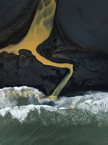 Aerial view of a river s golden tendrils snaking through the stark volcanic sands to meet the frothy turbulent embrace of the sea Iceland Iceland. Aerial view of a river s golden tendrils snaking through the stark volcanic sands to meet the frothy turbulent embrace of the sea Iceland Iceland.