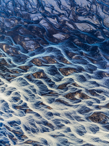 Aerial view of a complex network of glacial river channels with dark volcanic sediment and blue water flowing through the landscape of Iceland. Aerial view of a complex network of glacial river channels with dark volcanic sediment and blue water flowing through the landscape of Iceland.