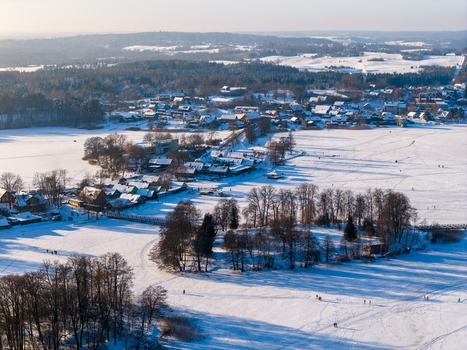 Aerial view of snow covered houses and bare trees in the town of Trakai along the shores of a frozen lake with people walking on the ice in Lithuania. Aerial view of snow covered houses and bare trees in the town of Trakai along the shores of a frozen lake with people walking on the ice in Lithuania.