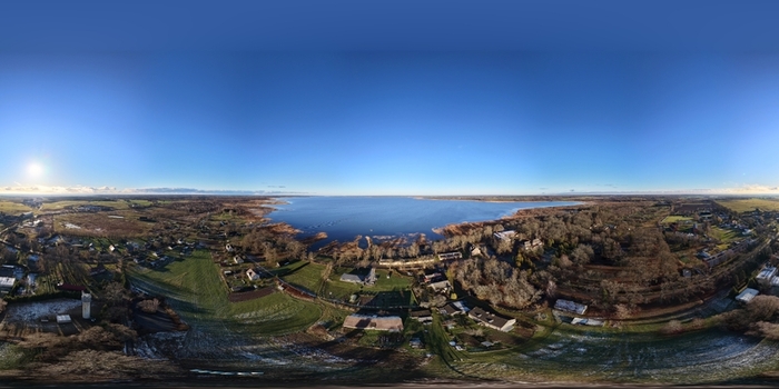 Aerial view of Lake Burtnieks surrounded by rural fields forests and small settlements under a clear blue sky in Burtnieki Valmiera Municipality Latvia.