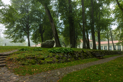 View of the lush park grounds of Taujenai Manor featuring a stone path mossy stone wall and tall trees Taujenai Vilnius County Lithuania.