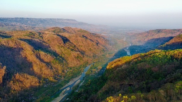 Aerial view of Kebun Buah Mangunan with a winding river flowing through lush hills under golden hour light in Kecamatan Dlingo Daerah Istimewa Yogya Indonesia.