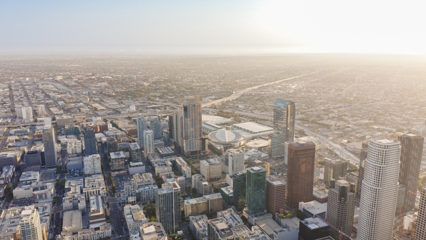 Aerial view of the Los Angeles skyline featuring modern skyscrapers dense urban development and highways under a bright sky in Los Angeles California United States.