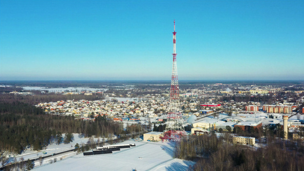 Aerial view of a tall red and white lattice radio tower standing in a snow covered landscape with a small town and forest in the background under a clear blue sky in Latvia. Aerial view of a tall red and white lattice radio tower standing in a snow covered landscape with a small town and forest in the background under a clear blue sky in Latvia.
