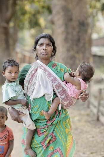 Odisha India 26 March 2026 View of a mother in a vibrant green sari carrying two children one nestled in a sling against a backdrop of earthy tones. Odisha India 26 March 2026 View of a mother in a vibrant green sari carrying two children one nestled in a sling against a backdrop of earthy tones.