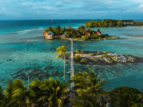 Aerial view of a tropical motu with red roofed bungalows and a long wooden bridge over turquoise waters in Moorea Maiao Windward Islands French Polynesia. Aerial view of a tropical motu with red roofed bungalows and a long wooden bridge over turquoise waters in Moorea Maiao Windward Islands French Polynesia.