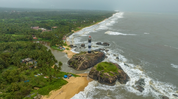 Aerial view of Kapu Light House standing on rocky outcrops surrounded by the Arabian Sea sandy beach and lush palm trees in Udupi Karnataka India.