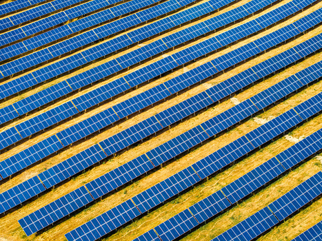 Aerial view of a modern solar park with rows of blue photovoltaic panels arranged on dry golden brown ground in Germany.