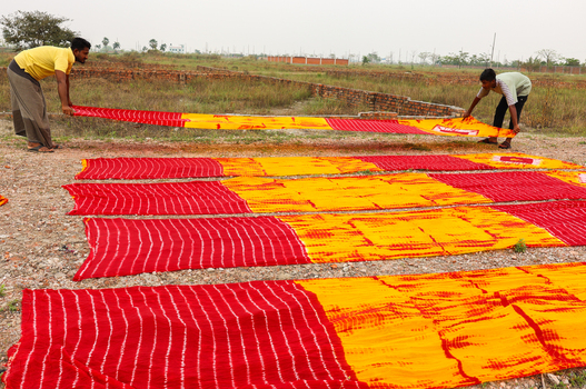 Narayanganj Bangladesh 30 March 2026 View of vibrant red and yellow fabrics laid out to dry under the open sky contrasting against the earthy tones of the field.